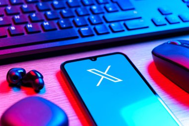 Prague, Czechia - 08 12 2025: A side view of a desk with a keyboard and a mobile phone displaying the X logo. X is a platform for sharing short posts and updates.