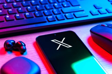 Prague, Czechia - 08 12 2025: A side view of a desk with a keyboard and a mobile phone displaying the X logo. X is a platform for sharing short posts and updates.
