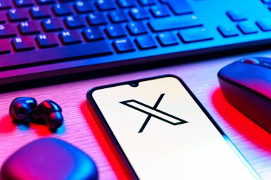 Prague, Czechia - 08 12 2025: A side view of a desk with a keyboard and a mobile phone displaying the X logo. X is a platform for sharing short posts and updates.