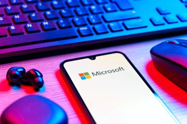 Prague, Czechia - 08 12 2025: A side view of a desk with a keyboard and a mobile phone displaying the Microsoft logo. Microsoft is a technology company offering software, hardware, and services.