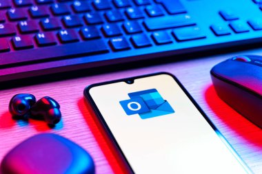 Prague, Czechia - 08 12 2025: A side view of a desk with a keyboard and a mobile phone displaying the Outlook logo. Outlook is an email platform for sending and managing messages.