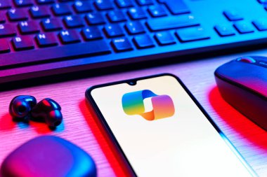 Prague, Czechia - 08 12 2025: A side view of a desk with a keyboard and a mobile phone displaying the Copilot logo. Copilot is an AI assistant integrated into software for productivity help.