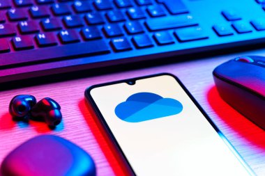 Prague, Czechia - 08 12 2025: A side view of a desk with a keyboard and a mobile phone displaying the OneDrive logo. OneDrive is a cloud storage platform for saving and sharing files.