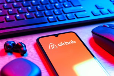 Prag, Çek Cumhuriyeti - 08 12 2025: Airbnb logosunu gösteren klavyesi ve cep telefonu olan bir masanın yan görüntüsü. Airbnb dünya çapında kısa vadeli konaklama için bir platformdur..