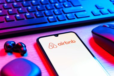 Prag, Çek Cumhuriyeti - 08 12 2025: Airbnb logosunu gösteren klavyesi ve cep telefonu olan bir masanın yan görüntüsü. Airbnb dünya çapında kısa vadeli konaklama için bir platformdur..