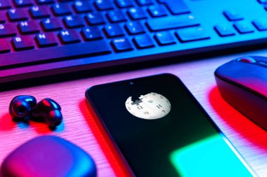 Prag, Çek Cumhuriyeti - 08 12 2025: Vikipedi logosunu gösteren klavyesi ve cep telefonu olan bir masanın yan görüntüsü. Vikipedi çevrimiçi bir ansiklopedidir..