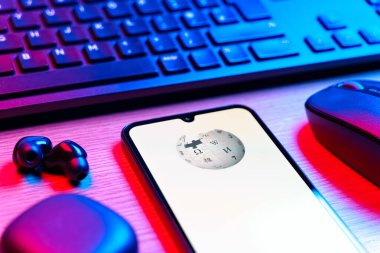 Prag, Çek Cumhuriyeti - 08 12 2025: Vikipedi logosunu gösteren klavyesi ve cep telefonu olan bir masanın yan görüntüsü. Vikipedi çevrimiçi bir ansiklopedidir..