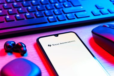 Prag, Çek Cumhuriyeti - 08 12 2025: Texas Instruments logosunu gösteren klavyesi ve cep telefonu olan bir masanın yan görüntüsü. Texas Instruments yarı iletken ve elektronik üreten bir şirket..