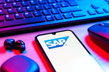 Prag, Çek Cumhuriyeti - 08 12 2025: SAP logosunu gösteren klavyesi ve cep telefonu olan bir masanın yan görüntüsü. SAP, şirket uygulamaları ve çözümleri sağlayan bir yazılım şirketidir..
