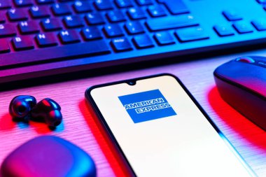 Prag, Çek Cumhuriyeti - 08 12 2025: Amerikan Ekspres logosunu gösteren klavyesi ve cep telefonu olan bir masanın yan görüntüsü. American Express kart ve bankacılık sunan bir finans şirketidir..