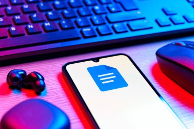 Prag, Çek Cumhuriyeti - 08 12 2025: Google Docs logosunu gösteren klavyesi ve cep telefonu olan bir masanın yan görüntüsü. Google Docs metin belgeleri oluşturmak ve düzenlemek için bir platformdur.