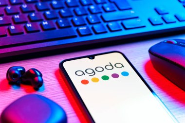 Prag, Çek Cumhuriyeti - 08 12 2025: Agoda logosunu gösteren klavyesi ve cep telefonu olan bir masanın yan görüntüsü. Agoda, otelleri ve seyahat yerlerini ayırtmak için bir platform..