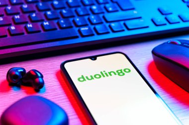 Prag, Çek Cumhuriyeti - 08 12 2025: Duolingo logosunu gösteren klavyesi ve cep telefonu olan bir masanın yan görüntüsü. Duolingo interaktif olarak dil öğrenmek için bir platformdur..