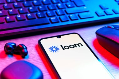 Prag, Çek Cumhuriyeti - 08 12 2025: Loom logosunu gösteren klavyeli ve cep telefonlu bir masanın yan görüntüsü. Loom video mesajlarını kaydetmek ve paylaşmak için bir platformdur.