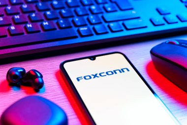 Prag, Çek Cumhuriyeti - 08 12 2025: Foxconn logosunu gösteren klavyesi ve cep telefonu olan bir masanın yan görüntüsü. Foxconn elektronik ve parça üreten bir şirket..