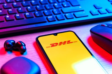 Prag, Çek Cumhuriyeti - 08 12 2025: DHL logosunu gösteren klavyesi ve cep telefonu olan bir masanın yan görüntüsü. DHL uluslararası nakliye hizmeti sunan bir lojistik şirketidir..