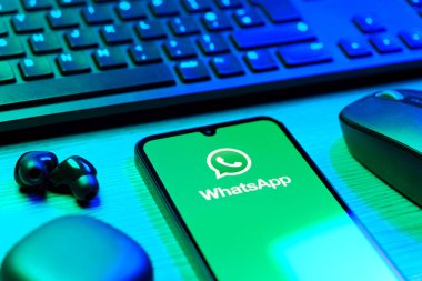 Prague, Czechia - 08 12 2025: A side view of a desk with a keyboard and a mobile phone displaying the WhatsApp logo. WhatsApp is an app for sending texts, calls, and media.