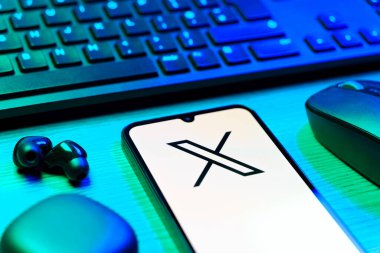 Prague, Czechia - 08 12 2025: A side view of a desk with a keyboard and a mobile phone displaying the X logo. X is a platform for sharing short posts and updates.