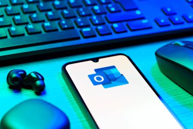 Prague, Czechia - 08 12 2025: A side view of a desk with a keyboard and a mobile phone displaying the Outlook logo. Outlook is an email platform for sending and managing messages.