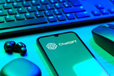 Prague, Czechia - 08 12 2025: A side view of a desk with a keyboard and a mobile phone displaying the ChatGPT logo. ChatGPT is an AI chatbot for generating text and answering questions.