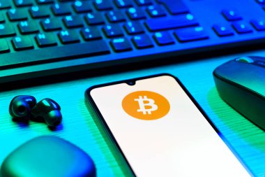 Prag, Çek Cumhuriyeti - 08 12 2025: Bitcoin logosunu gösteren klavyesi ve cep telefonu olan bir masanın yan görüntüsü. Bitcoin merkezi olmayan işlemler için dijital bir kripto para birimidir.