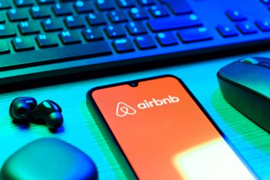 Prag, Çek Cumhuriyeti - 08 12 2025: Airbnb logosunu gösteren klavyesi ve cep telefonu olan bir masanın yan görüntüsü. Airbnb dünya çapında kısa vadeli konaklama için bir platformdur..