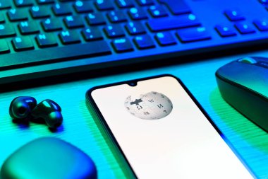 Prag, Çek Cumhuriyeti - 08 12 2025: Vikipedi logosunu gösteren klavyesi ve cep telefonu olan bir masanın yan görüntüsü. Vikipedi çevrimiçi bir ansiklopedidir..