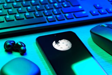 Prag, Çek Cumhuriyeti - 08 12 2025: Vikipedi logosunu gösteren klavyesi ve cep telefonu olan bir masanın yan görüntüsü. Vikipedi çevrimiçi bir ansiklopedidir..
