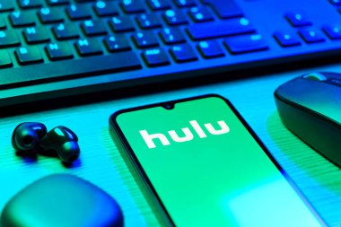 Prag, Çek Cumhuriyeti - 08 12 2025: Hulu logosunu gösteren klavyesi ve cep telefonu olan bir masanın yan görüntüsü. Hulu TV şovları, filmler ve canlı TV için bir yayın platformu..