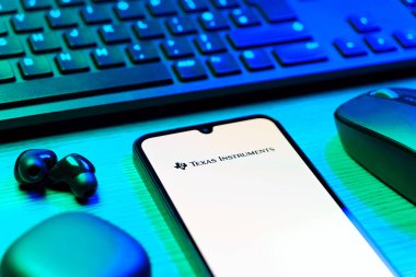 Prag, Çek Cumhuriyeti - 08 12 2025: Texas Instruments logosunu gösteren klavyesi ve cep telefonu olan bir masanın yan görüntüsü. Texas Instruments yarı iletken ve elektronik üreten bir şirket..