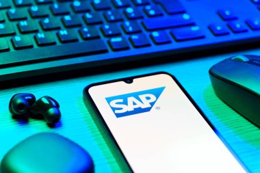 Prag, Çek Cumhuriyeti - 08 12 2025: SAP logosunu gösteren klavyesi ve cep telefonu olan bir masanın yan görüntüsü. SAP, şirket uygulamaları ve çözümleri sağlayan bir yazılım şirketidir..