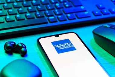 Prag, Çek Cumhuriyeti - 08 12 2025: Amerikan Ekspres logosunu gösteren klavyesi ve cep telefonu olan bir masanın yan görüntüsü. American Express kart ve bankacılık sunan bir finans şirketidir..
