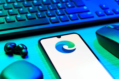 Prag, Çek Cumhuriyeti - 08 12 2025: Kenar logosunu gösteren klavyesi ve cep telefonu olan bir masanın yan görüntüsü. Edge, Microsoft tarafından Windows aygıtları için geliştirilen bir web tarayıcısıdır..