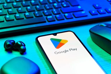 Prag, Çek Cumhuriyeti - 08 12 2025: Google Play logosunu gösteren klavyesi ve cep telefonu olan bir masanın yan görüntüsü. Google Play uygulamaları, oyunları ve dijital içeriği indirmek için bir platformdur.