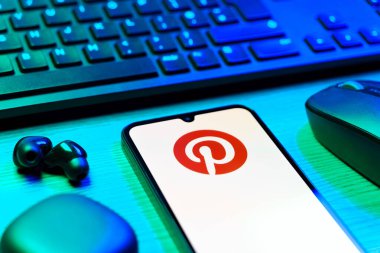 Prag, Çek Cumhuriyeti - 08 12 2025: Pinterest logosunu gösteren klavyesi ve cep telefonu olan bir masanın yan görüntüsü. Pinterest fikirleri görsel olarak keşfetmek ve kaydetmek için bir platformdur..