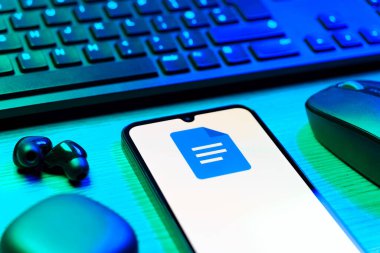 Prag, Çek Cumhuriyeti - 08 12 2025: Google Docs logosunu gösteren klavyesi ve cep telefonu olan bir masanın yan görüntüsü. Google Docs metin belgeleri oluşturmak ve düzenlemek için bir platformdur.