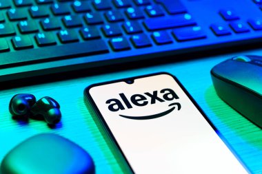 Prag, Çek Cumhuriyeti - 08 12 2025: Alexa logosunu gösteren klavyesi ve cep telefonu olan bir masanın yan görüntüsü. Alexa akıllı aygıtlar ve servisler için ses asistanıdır.