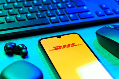 Prag, Çek Cumhuriyeti - 08 12 2025: DHL logosunu gösteren klavyesi ve cep telefonu olan bir masanın yan görüntüsü. DHL uluslararası nakliye hizmeti sunan bir lojistik şirketidir..