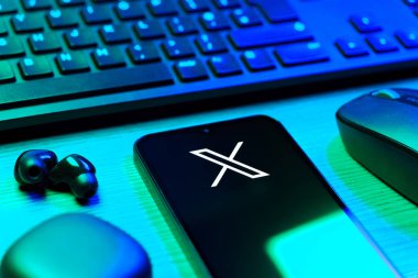 Prague, Czechia - 08 12 2025: A side view of a desk with a keyboard and a mobile phone displaying the X logo. X is a platform for sharing short posts and updates.