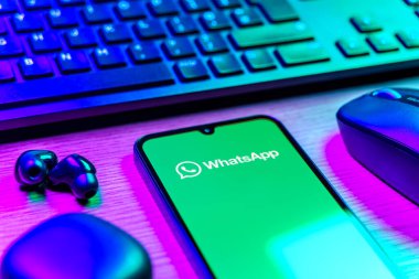 Prague, Czechia - 08 12 2025: A side view of a desk with a keyboard and a mobile phone displaying the WhatsApp logo. WhatsApp is an app for sending texts, calls, and media.
