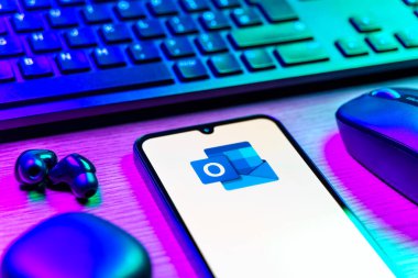 Prague, Czechia - 08 12 2025: A side view of a desk with a keyboard and a mobile phone displaying the Outlook logo. Outlook is an email platform for sending and managing messages.