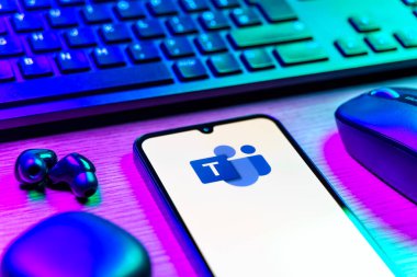 Prague, Czechia - 08 12 2025: A side view of a desk with a keyboard and a mobile phone displaying the Teams logo. Teams is a platform for team collaboration, meetings, and communication.