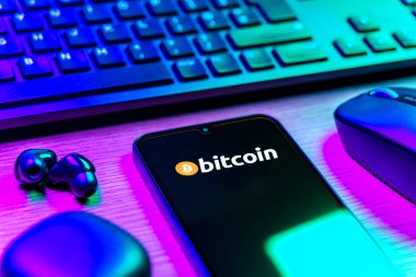 Prag, Çek Cumhuriyeti - 08 12 2025: Bitcoin logosunu gösteren klavyesi ve cep telefonu olan bir masanın yan görüntüsü. Bitcoin merkezi olmayan işlemler için dijital bir kripto para birimidir.