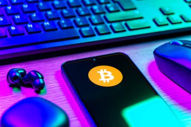 Prag, Çek Cumhuriyeti - 08 12 2025: Bitcoin logosunu gösteren klavyesi ve cep telefonu olan bir masanın yan görüntüsü. Bitcoin merkezi olmayan işlemler için dijital bir kripto para birimidir.