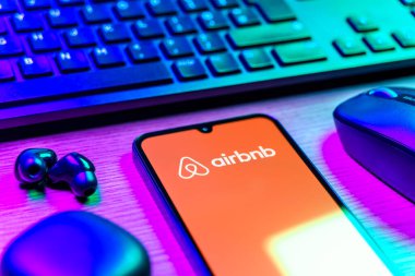 Prag, Çek Cumhuriyeti - 08 12 2025: Airbnb logosunu gösteren klavyesi ve cep telefonu olan bir masanın yan görüntüsü. Airbnb dünya çapında kısa vadeli konaklama için bir platformdur..
