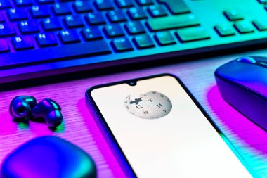Prag, Çek Cumhuriyeti - 08 12 2025: Vikipedi logosunu gösteren klavyesi ve cep telefonu olan bir masanın yan görüntüsü. Vikipedi çevrimiçi bir ansiklopedidir..