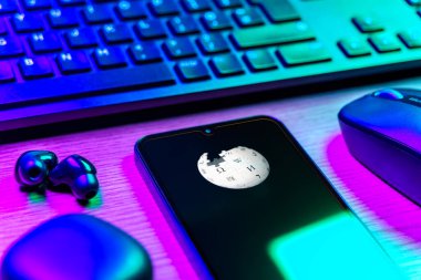 Prag, Çek Cumhuriyeti - 08 12 2025: Vikipedi logosunu gösteren klavyesi ve cep telefonu olan bir masanın yan görüntüsü. Vikipedi çevrimiçi bir ansiklopedidir..