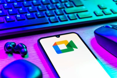 Prag, Çek Cumhuriyeti - 08 12 2025: Google Meet logosunu gösteren klavyesi ve cep telefonu olan bir masanın yan görüntüsü. Google Meet video toplantıları ve çevrimiçi işbirliği için bir platformdur.