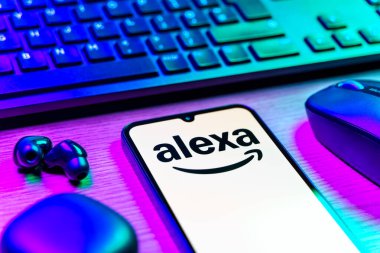 Prag, Çek Cumhuriyeti - 08 12 2025: Alexa logosunu gösteren klavyesi ve cep telefonu olan bir masanın yan görüntüsü. Alexa akıllı aygıtlar ve servisler için ses asistanıdır.