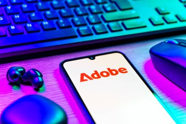 Prag, Çek Cumhuriyeti - 08 12 2025: Adobe logosunu gösteren klavyeli ve cep telefonlu bir masanın yan görüntüsü. Adobe yaratıcı araçlar ve hizmetler sunan bir yazılım şirketidir..